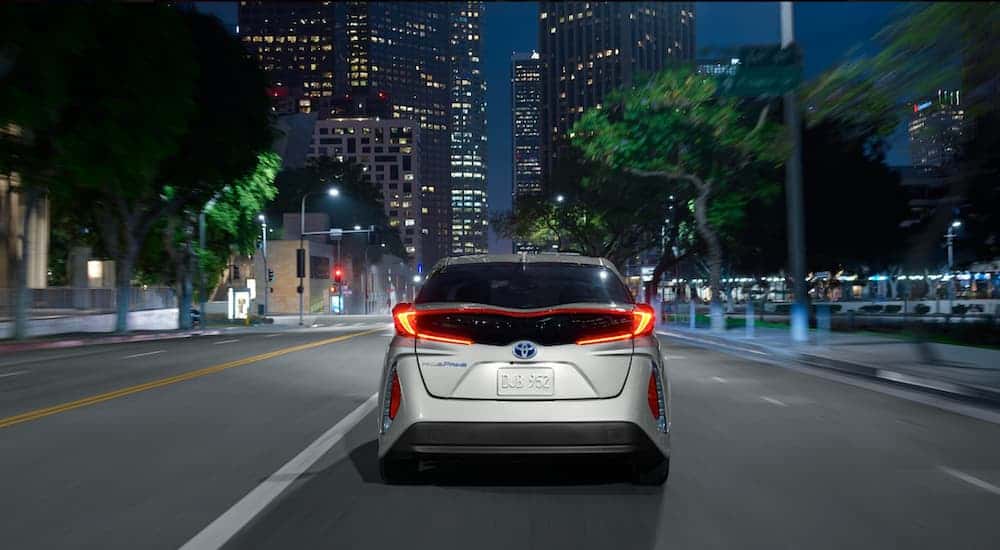 A silver 2021 Toyota Prius Prime LE is shown from the rear driving down a city street.
