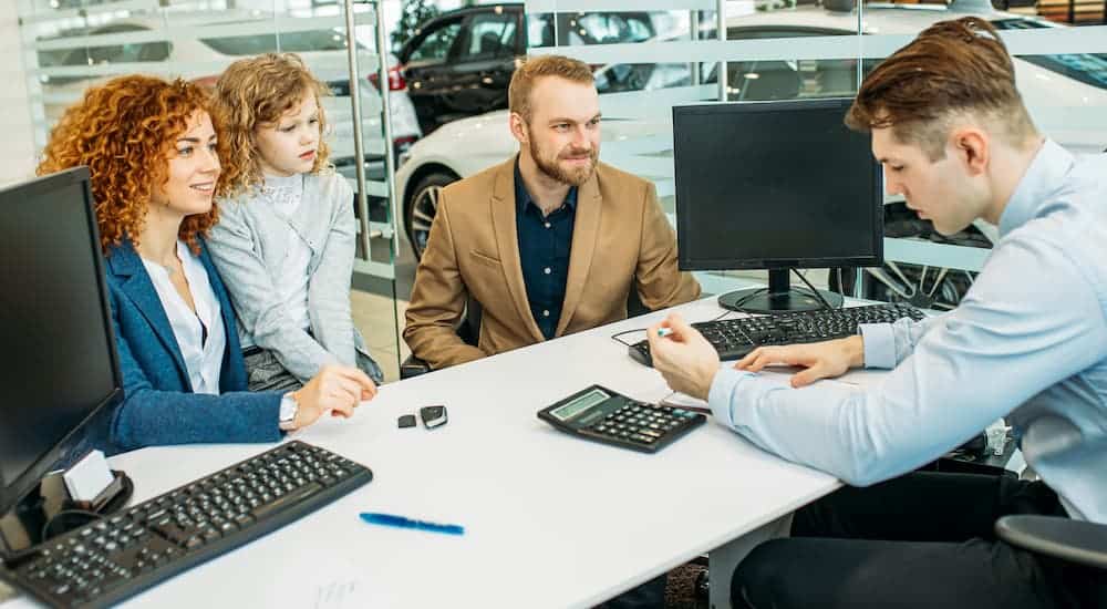 A car salesman is going over financing paperwork with a family at the Chevy dealer.