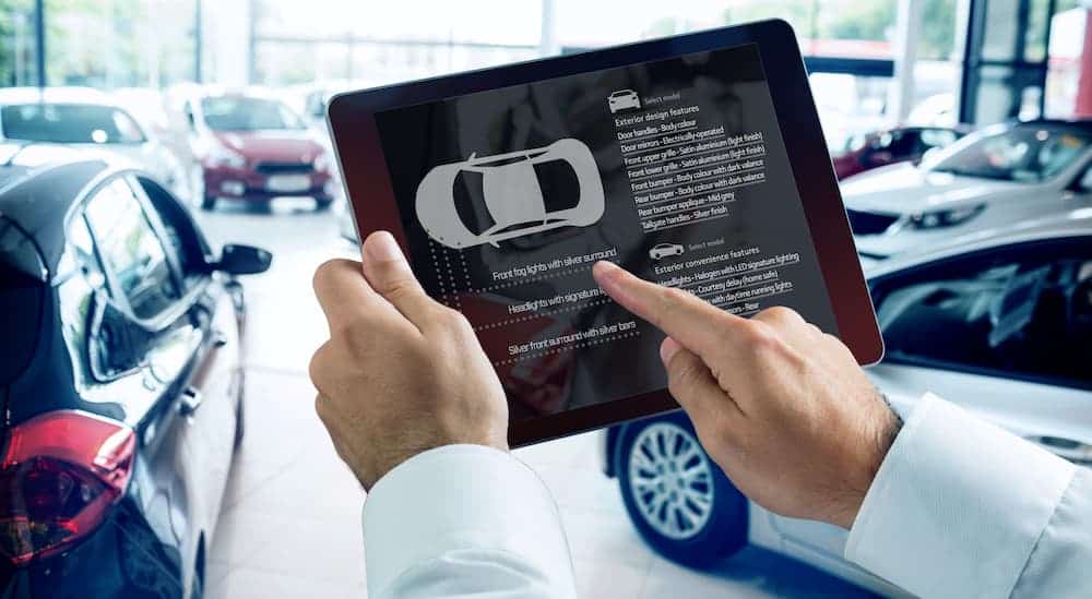 A man is holding a tablet with a car silhouette and features displayed on the screen.