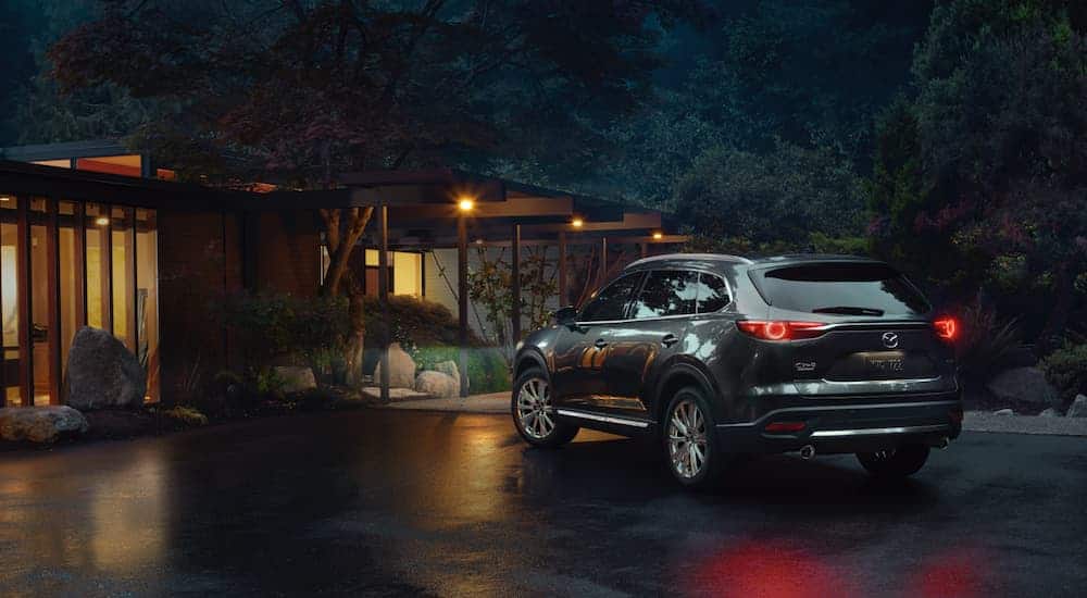 A grey 2021 Mazda CX-5 is sown from the rear angled left parked outside a modern house at night.