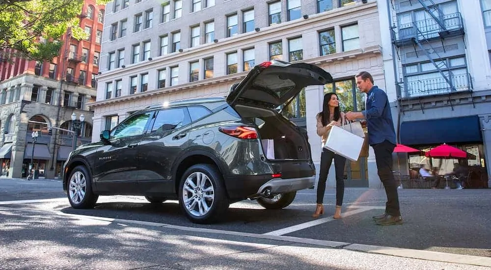 A grey 2021 Chevy Blazer is parked in the city where a couple is loading shopping bags into the back.