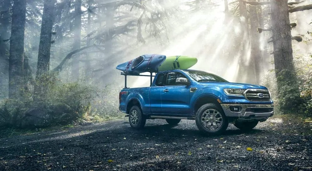 A blue 2020 Ford Ranger Lariat FX4 is parked in the woods with a blue and a green kayak mounted over the bed.