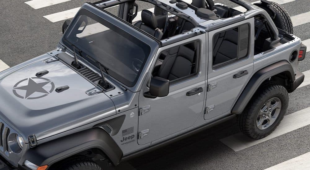 A silver 2021 Jeep Wrangler Freedom Edition is driving over a crosswalk.