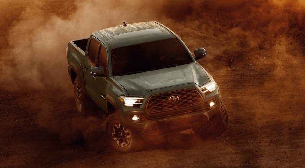 A green 2021 Toyota Tacoma is driving down a dirt path with a bunch of dust in the air.
