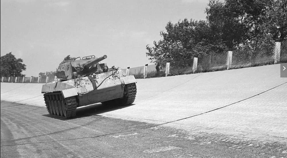A 1942 M18 Hellcat Tank is shown in black and white driving down a wide road.