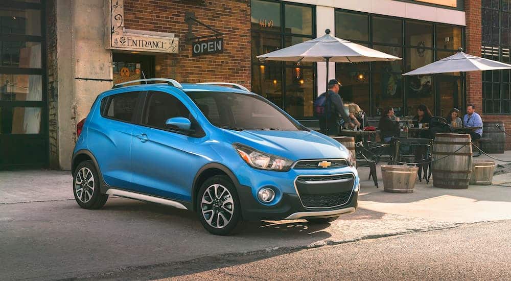 A blue 2018 Chevy Spark ACTIV is parked outside of a restaurant.