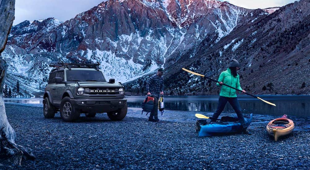 A grey 2021 Ford Bronco is parked on a river bed where a couple is prepping to kayak.