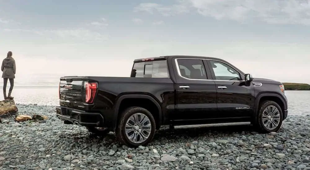 A woman is standing next to her black 2020 GMC Sierra 1500, which is a popular option among GMC trucks, that's parked on rocks next to a lake. 