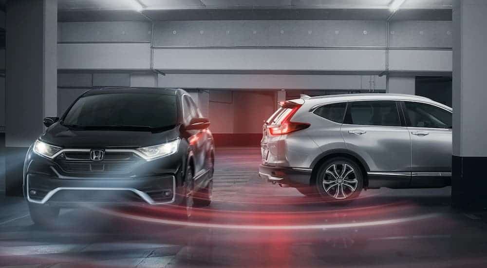 A white 2020 Honda CR-V is backing up in a parking garage showing cross traffic safety features.