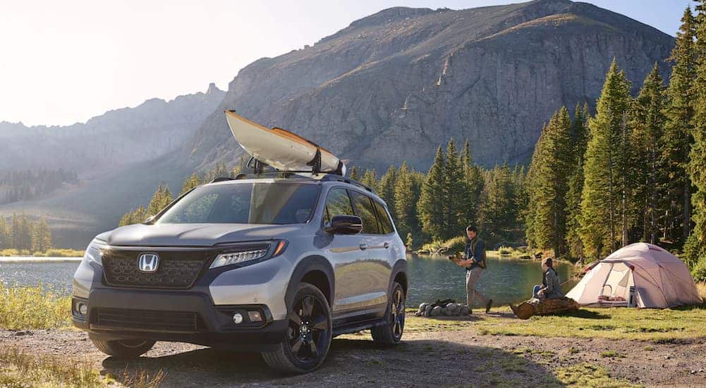 A silver 2021 Honda Passport is parked at a campsite with a kayak on the roof.
