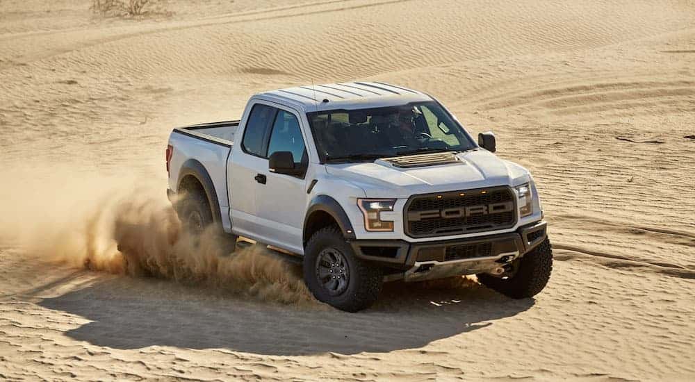 A white 2017 used Ford F-150 Raptor is driving in the desert kicking up sand.