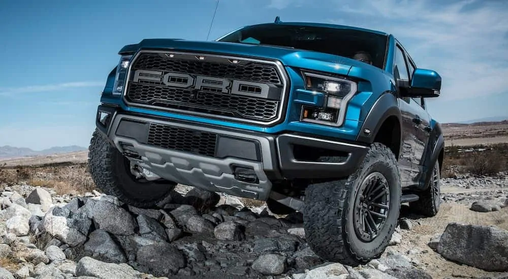 A blue 2020 used Ford F-150 Raptor is crawling over some rocks.