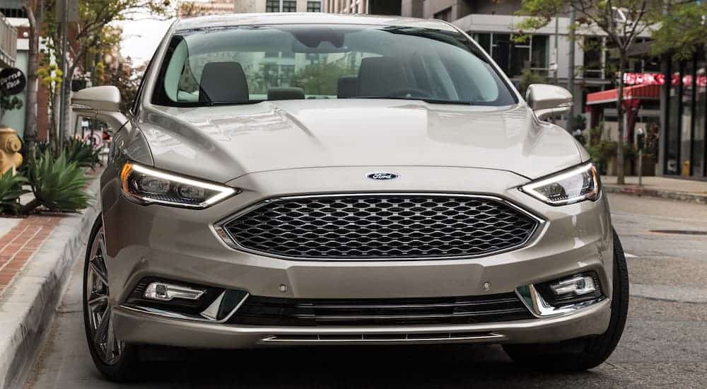A tan 2017 used Ford Fusion Hybrid Platinum is parked on the street, shown from the front.