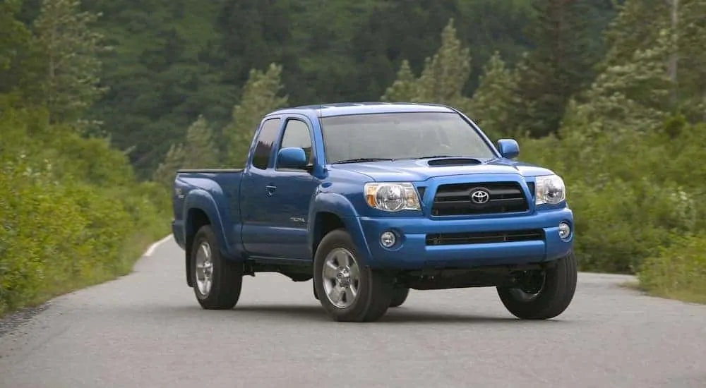 A blue 2007 used Toyota Tacoma is parked angled right on a tree lined road.