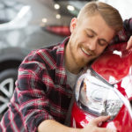 A man happily hugging his red car in a dealership