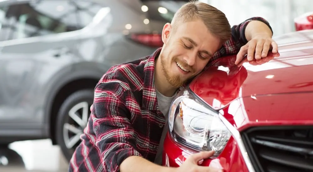 A man happily hugging his red car in a dealership