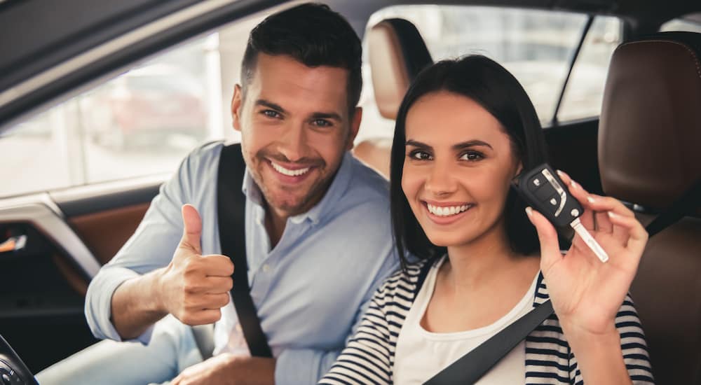 An excited couple giving a thumbs up in their new car