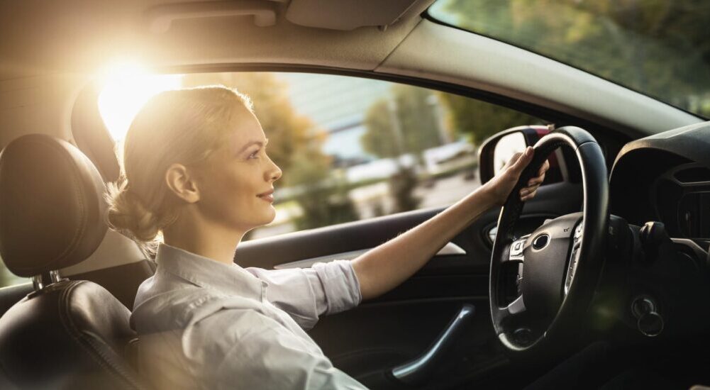 A woman is shown driving a car through a sunny city.