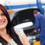 Happy woman standing in front of her repaired vehicle at a local dealership