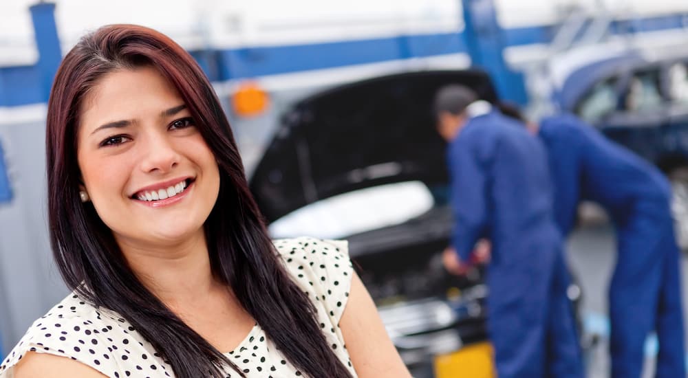 Happy woman standing in front of her repaired vehicle at a local dealership