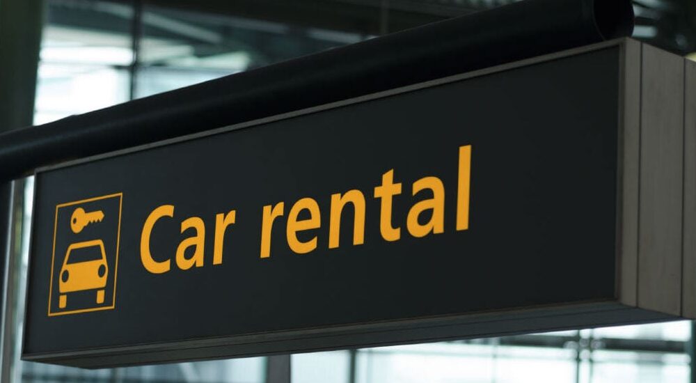 A black sign in an airport with the words "car rental" printed in orange text is shown.