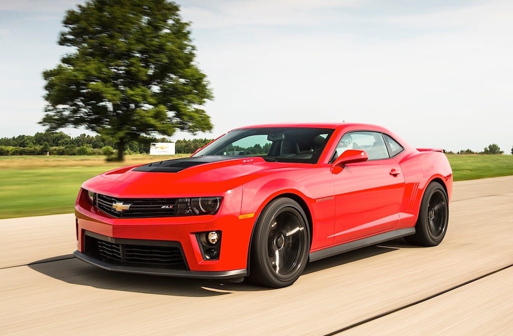 A red 2013 Chevrolet Camaro ZL1 driving on a road with a field in the back
