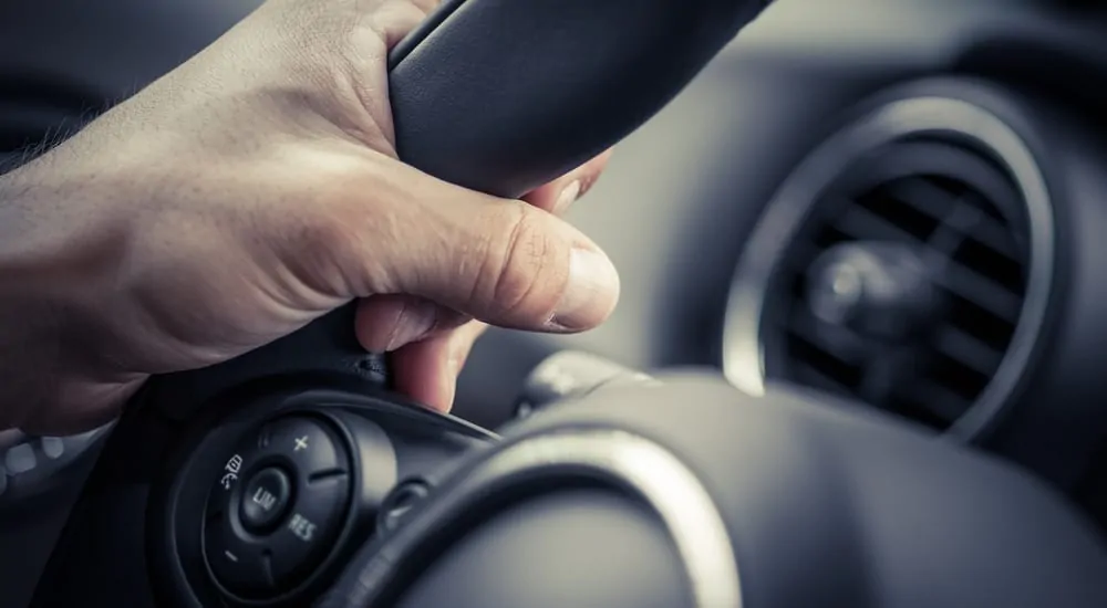 Close up of a hand wrapped around the top left of a black steering wheel