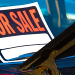 "For Sale" sign on the windshield of a black car with the hood open