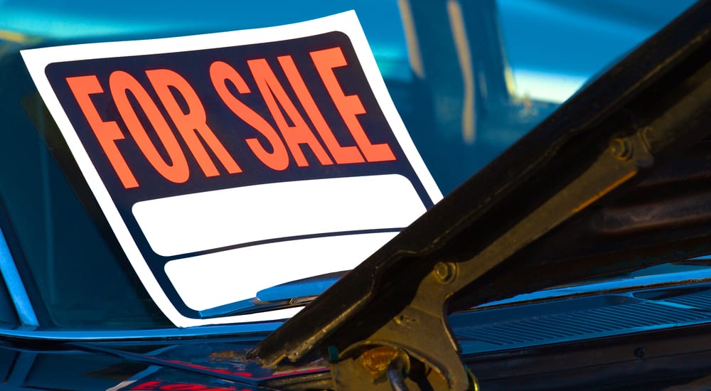 "For Sale" sign on the windshield of a black car with the hood open