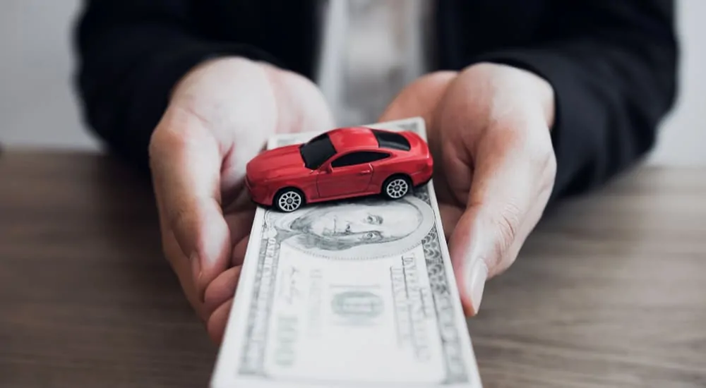 A man holding a stack of $100 bills with a red car on top