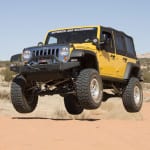 A yellow modified used Jeep Wrangler is jumping in the desert.