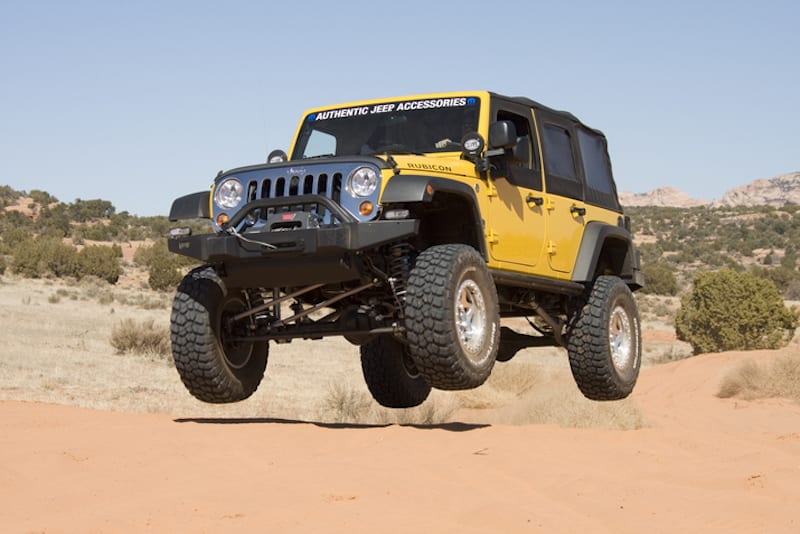 A yellow modified used Jeep Wrangler is jumping in the desert.