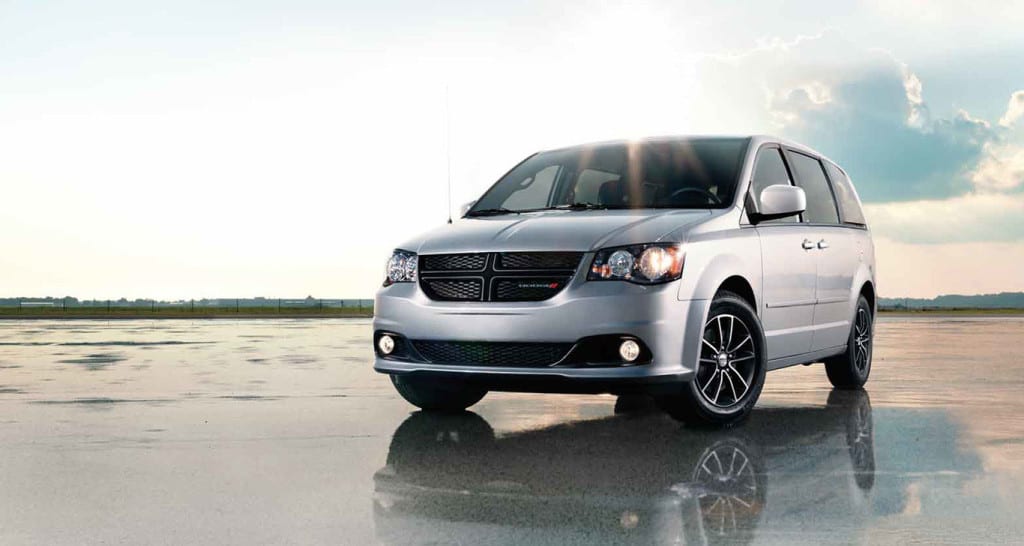 A silver 2015 Dodge Grand Caravan is parked in an open area against a cloudy sky.
