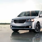 A silver 2015 Dodge Grand Caravan is parked in an open area against a cloudy sky.