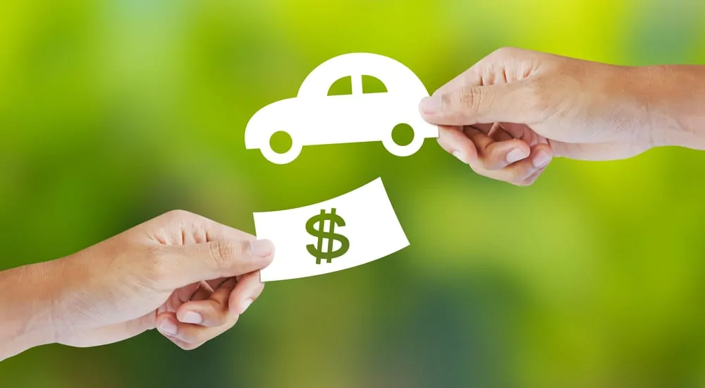 Green background with two hands on it, one holding a white silhouette of money, the other holding a white silhouette of a car