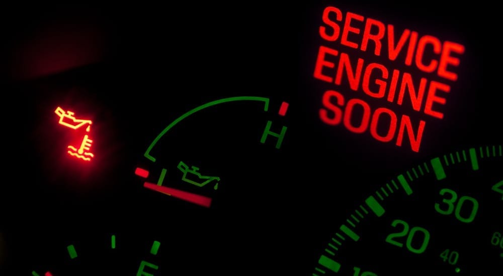 A close-up of an oil warning on a car's dashboard with the words "service engine soon" glowing in red text.