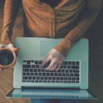 Man holding laptop and searching the web for AutoInfluence with coffee