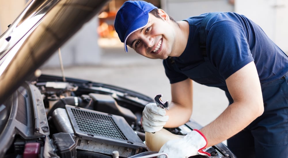 A smiling mechanic is shown performing an oil change on the engine of an open car.