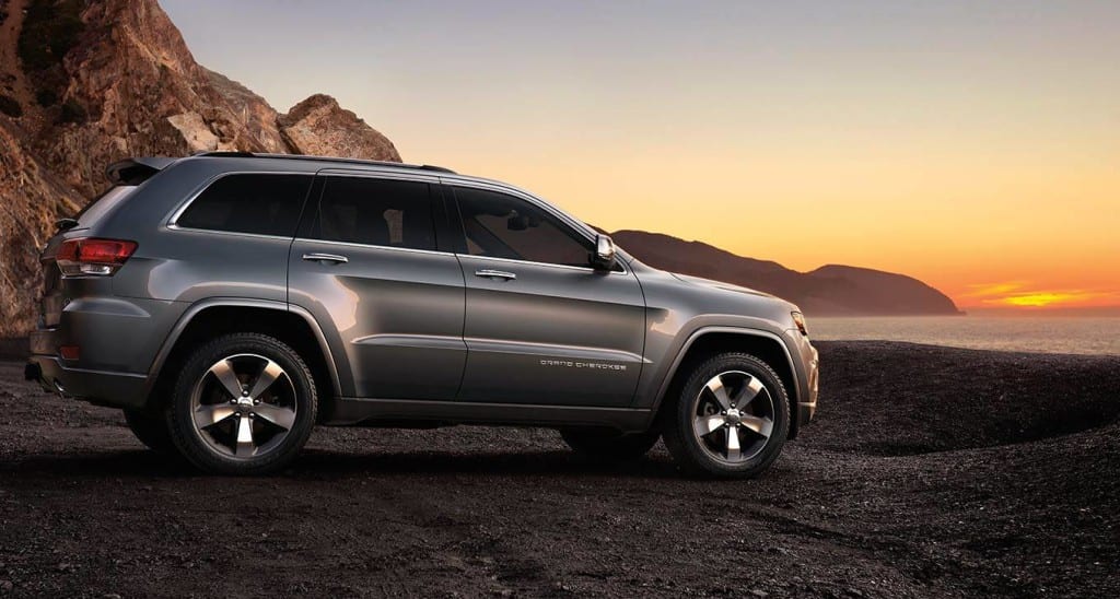 A silver 2014 Jeep Grand Cherokee with mountains in the back at sunset