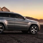 A silver 2014 Jeep Grand Cherokee with mountains in the back at sunset