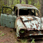 Old rusted mint-green car with the passenger door open, parked in the woods