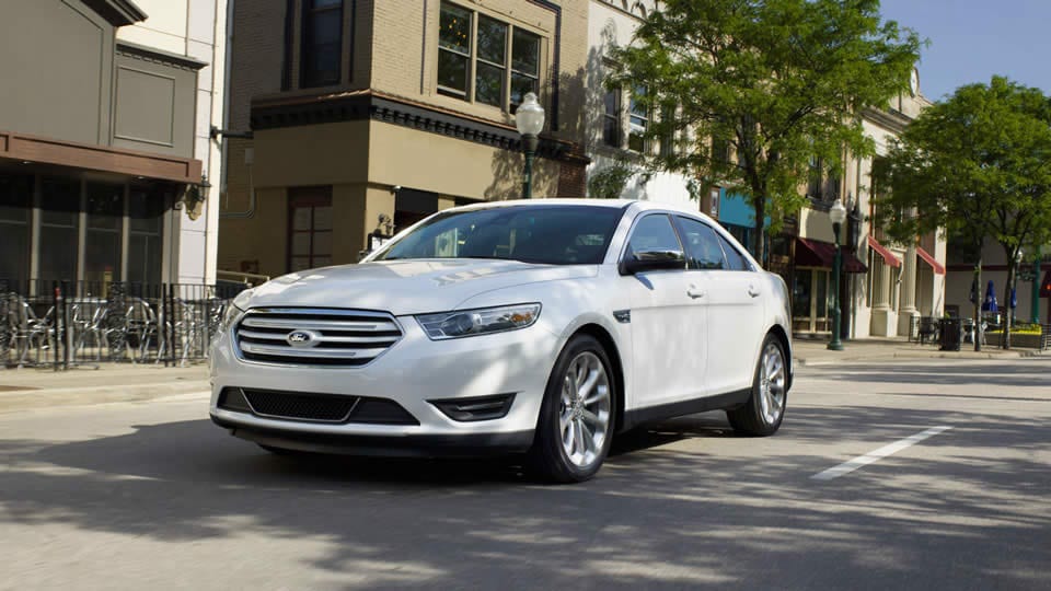 A white 2016 Ford Taurus is shown froma front angle on a city street after leaving a Ford dealer.