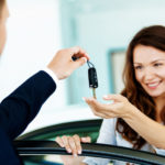 Man in a suit handing a woman car keys as she stands behind the car door