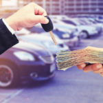 Hands in front of a row of vehicles, one holding a key and the other holding a stack of cash