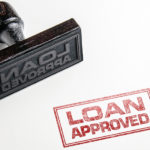 Black stamp laying on its side and red "loan approved" in front of it