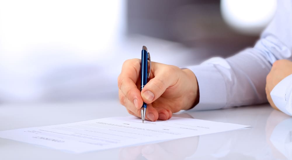 Man's hand holding a pen to a white form that is sitting on a white table