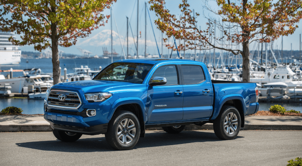 A blue 2018 Toyota Tacoma is parked in front of a bay with sailboats.