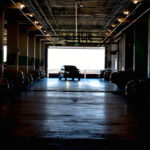 Dark parking garage with a single car alone being lit by daylight