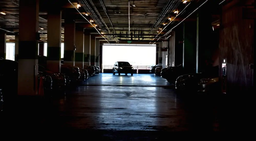 Dark parking garage with a single car alone being lit by daylight