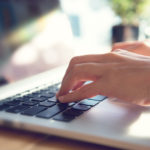 A man's hands typing on keyboard of laptop